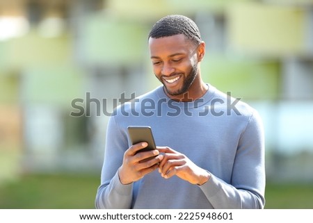 Happy black man checks cell phone walking in the street Royalty-Free Stock Photo #2225948601