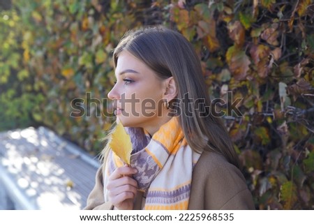 A girl with an autumn leaf in the park. A fashionable girl with a smile. Autumn mood.