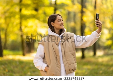 attractive young woman walking in autumn park taking selfie pictures with leaf using smartphone