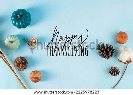 Top view of pumpkins and pine cones on blue background with Happy Thanksgiving text for holiday greeting in fall season.