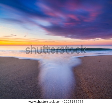 A seascape during sunset. Sand on the seashore. Bright sky during sunset. A sandy beach at low tide. Long exposure. Photo for wallpaper.
