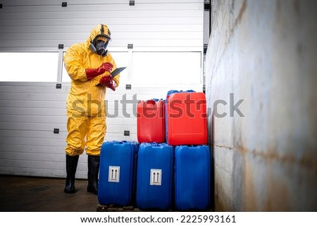 Professional worker in hazmat suit and gas mask checking inventory of chemicals in factory storage room. Royalty-Free Stock Photo #2225993161