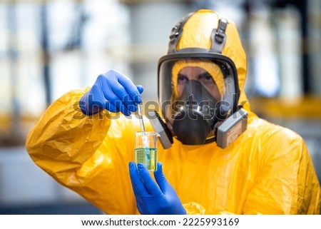 Professional chemical worker in protection suit and gas mask handling dangerous material inside chemicals production plant. Royalty-Free Stock Photo #2225993169