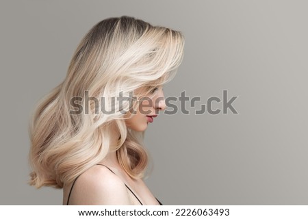 Young beautiful blonde woman on a gray background. Beautiful wavy shiny hair.