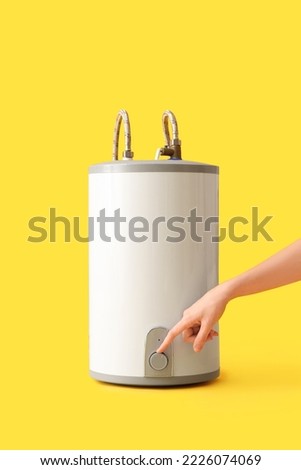 Woman adjusting electric boiler on yellow background