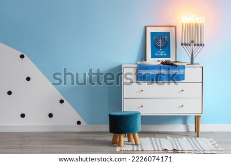 Plate with cookies, Torah, dreidels, menorah and picture on chest of drawers near blue wall
