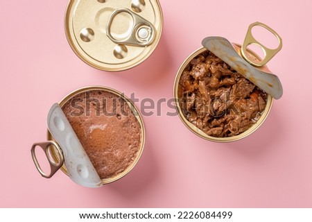 Wet cat food in open jars over pastel pink background. Wet pet feed in metal cans closeup. Canned meat pieces and soft pate for carnivore domestic animals. Сat food concept. Top view. Royalty-Free Stock Photo #2226084499