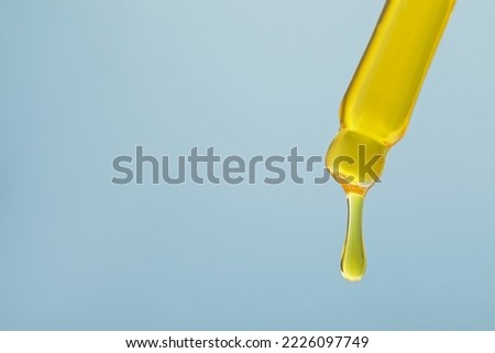 Dripping yellow serum from pipette on grey background, closeup. Space for text