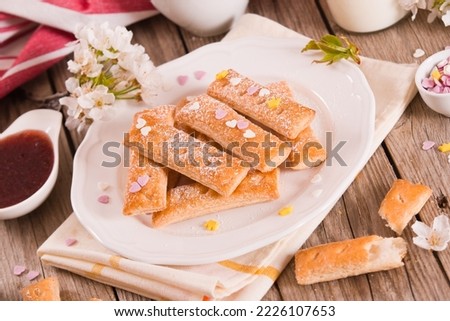 Puff pastry cookies with icing sugar on white dish.