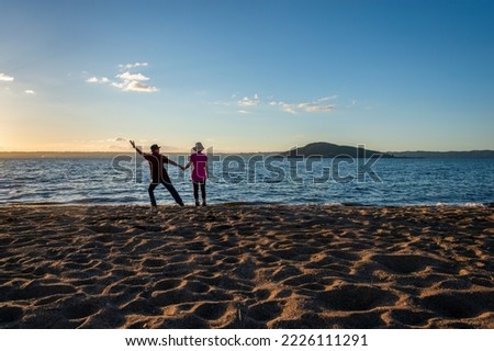 Tourists raising arm and enjoying lake Rotorua at sunset, Mokoia Island in the distance, Rotorua.