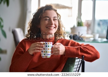 Young smiling pretty woman holding cup drinking warm tea or coffee relaxing dreaming at home. Happy positive lady enjoying hot drink daydreaming with mug in hands in cold cozy winter weekend morning. Royalty-Free Stock Photo #2226115229