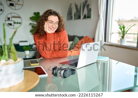 Young smiling pretty woman student using laptop elearning or remote working at home office looking at laptop computer watching webinar, learning web course, studying online sitting at table.