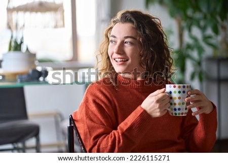 Young smiling pretty woman holding cup drinking warm tea or coffee relaxing dreaming at home. Happy positive calm lady enjoying hot drink with mug in hands daydreaming in cold cozy winter morning. Royalty-Free Stock Photo #2226115271