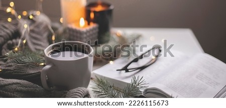 Banner image. Cozy home still life concept. Cup of hot coffee and opened book with atmospheric lights and burning candle. Winter holidays, Christmas time concept. Long banner for web site.