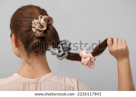 Woman with silk scrunchies on ponytail against grey background Royalty-Free Stock Photo #2226117841