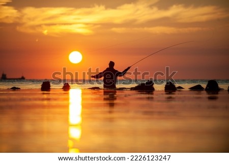 Rear view silhouette of man fishing with rod while standing in sea against cloudy sky during sunset