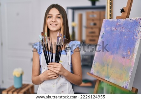 Adorable girl smiling confident holding paintbrushes at art studio Royalty-Free Stock Photo #2226124955