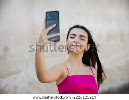 Portrait of beautiful dark-haired teenager woman wearing pink top, looking her mobile phone at summer