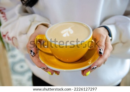 yellow cup of coffee in the hands of a girl