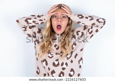 Horrible, stress, shock. Portrait emotional crazy caucasian teen girl wearing animal print sweater over white background clasping head in hands. Emotions, facial expression concept.