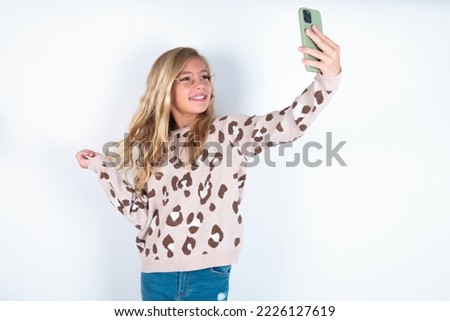 Portrait of a caucasian teen girl wearing animal print sweater over white background taking a selfie to send it to friends and followers or post it on his social media.