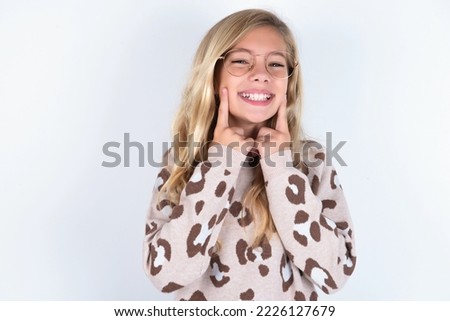 Strong healthy straight white teeth. Close up portrait of happy caucasian teen girl wearing animal print sweater over white background with beaming smile pointing on perfect clear white teeth.