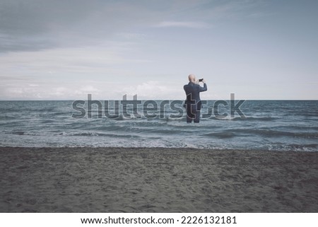 Businessman standing in the sea at the beach and taking pictures
