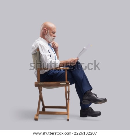Professional actor sitting on a director's chair and reading a screenplay: film industry, theater and drama school concept Royalty-Free Stock Photo #2226132207
