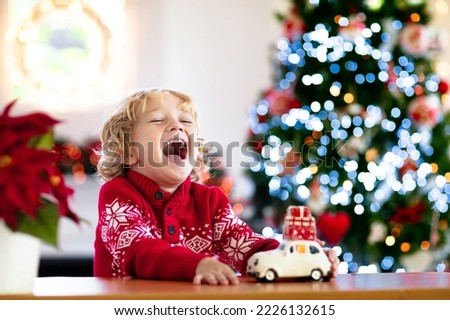 Child with Christmas present. Kid with Xmas gift. Little boy playing with a toy car under Christmas tree. Decorated home for winter holidays. Celebration with children. Kids play.