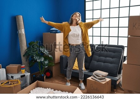 Young blonde woman smiling confident standing with arms open at new home