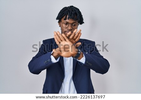 Young african man with dreadlocks wearing business jacket over white background rejection expression crossing arms and palms doing negative sign, angry face 