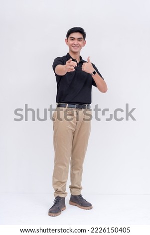 A friendly asian man points to the camera while smiling. Endorsing someone, making the thumbs up sign. Isolated on a white background.