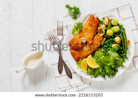 Crispy Beer Batter Cod Fish fillet with roast brussel sprouts, green beans, green peas and fresh lettuce on white plate on wood table,horizontal view from above, flat lay, free space