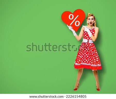 Woman holding red paper heart shape with % sign. Full length body portrait of happy pin up girl show pointing signboard. Sales ad concept. Green background. Valentine or like. Black Friday advertising