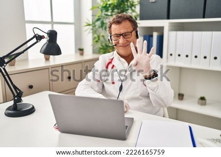 Senior doctor man working on online appointment showing and pointing up with fingers number four while smiling confident and happy. 