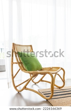 wooden rattan chair with green pillow beige carpet, with white curtain behind in sunny day