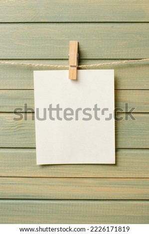 An empty piece of paper is hanging on a rope. A design element. Wooden background. Copy space.