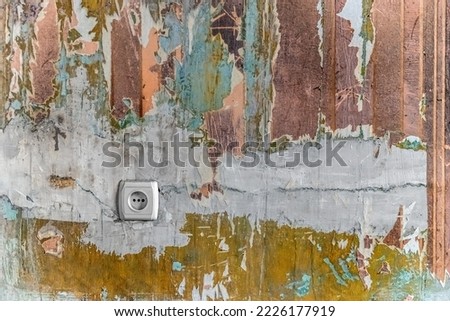 A wall in a room with tattered wallpaper, paint and plaster stains, and an European electrical outlet. Vintage grunge architectural-renovation background with copy space