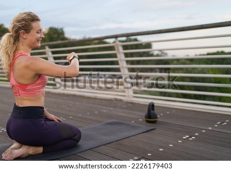 lateral view of Smiling young woman looking at her watch while exercising in the middle of town