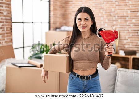 Young woman moving to a new home packing boxes smiling looking to the side and staring away thinking. 
