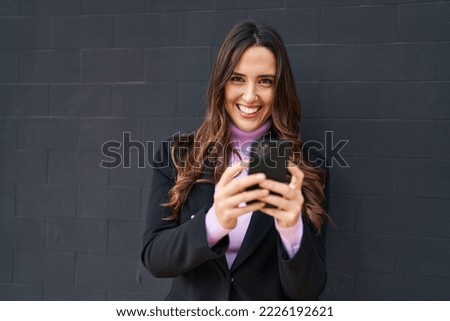 Young hispanic woman smiling confident using smartphone over black background