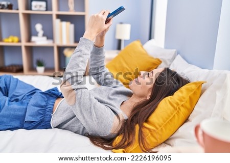 Young beautiful hispanic woman make selfie by smartphone lying on bed at bedroom