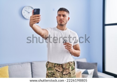 Young hispanic man wearing camouflage army uniform taking selfie at home skeptic and nervous, frowning upset because of problem. negative person. 