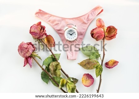 Pink dried rose, alarm clock and woman underwear. Concept of menopause, withered female beauty and the cessation of monthly menstrual cycles. World menopause day