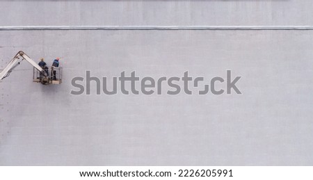 Two workers stand on the overpass and insulate the walls of the house.Banner.Copy space. Improvement of the facade of the house