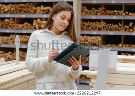 Woman with tablet in a timber and lumber warehouse or hardware store. Product acceptance and quality control. Worker woman expert and storekeeper. Royalty-Free Stock Photo #2226212297