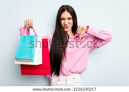 Young caucasian woman going to buy some clothes isolated on blue background showing a dislike gesture, thumbs down. Disagreement concept.