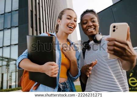 Young multiracial women smiling and taking selfie photo on cellphone at city street