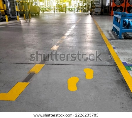 A walkway in an industrial building painted yellow footprints between parallel yellow lines on the abstract cement floor. Safety concept, negotiations on the pavement.