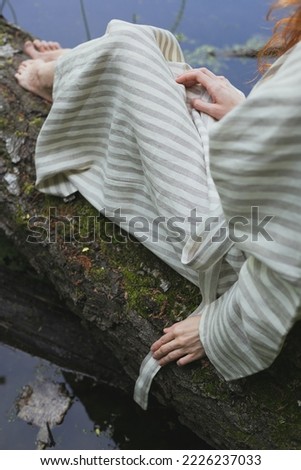 Close up lady sitting on log concept photo. Barefoot woman. Rustic clothing. Rear view photography with lake on background. High quality picture for wallpaper, travel blog, magazine, article
